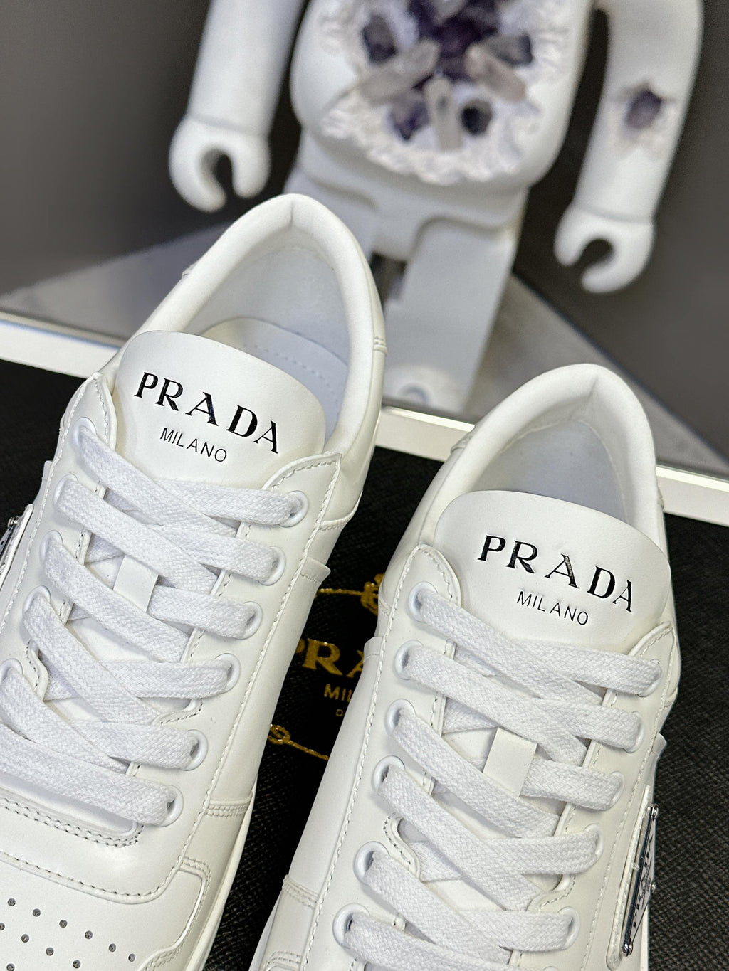 Pair of white leather Prada sneakers with PRADA MILANO branding on the tongues.