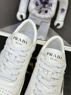 Pair of white leather Prada sneakers with PRADA MILANO branding on the tongues.