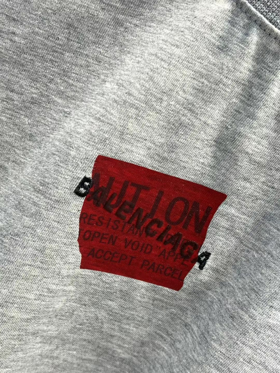 Light gray T-shirt with red logo patch and black text detail