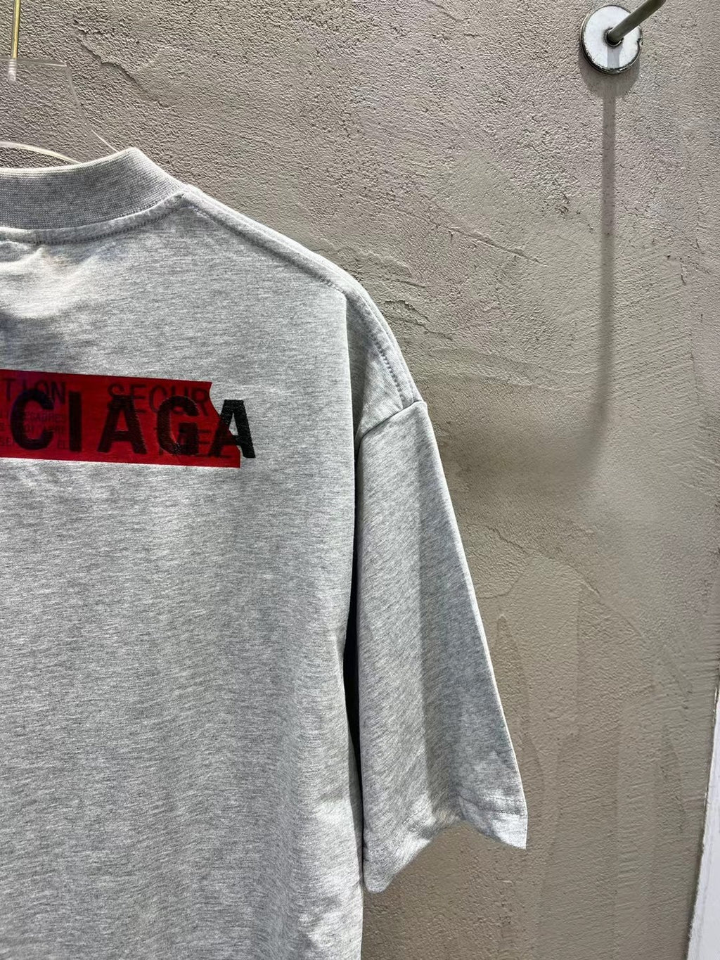 Light gray T-shirt with partial red logo lettering across the chest (side view)
