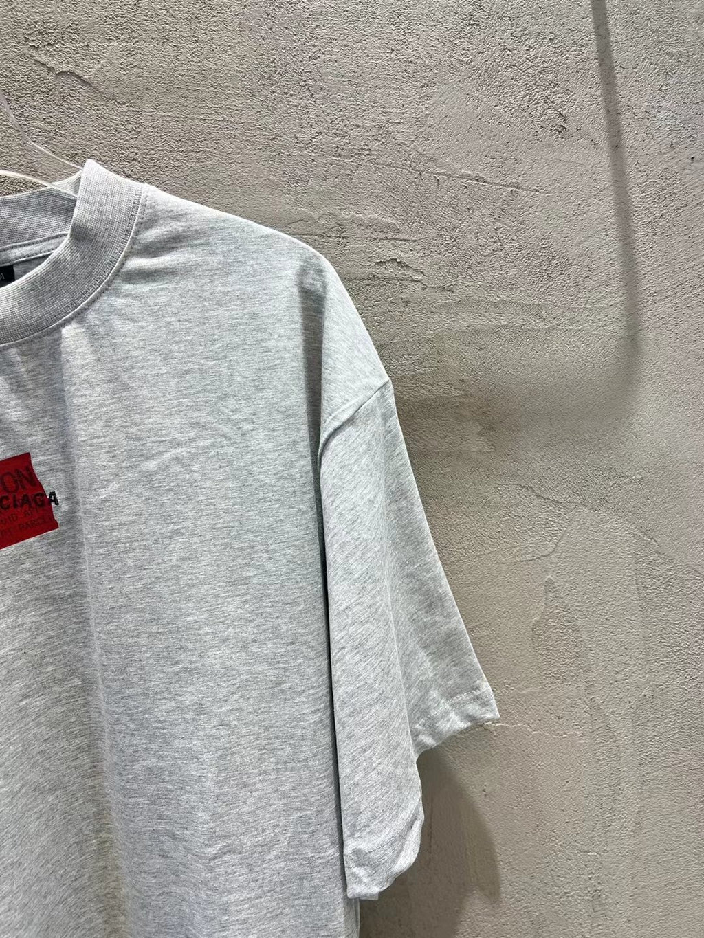 Light gray short-sleeve T-shirt with crewneck and red logo patch (side view)