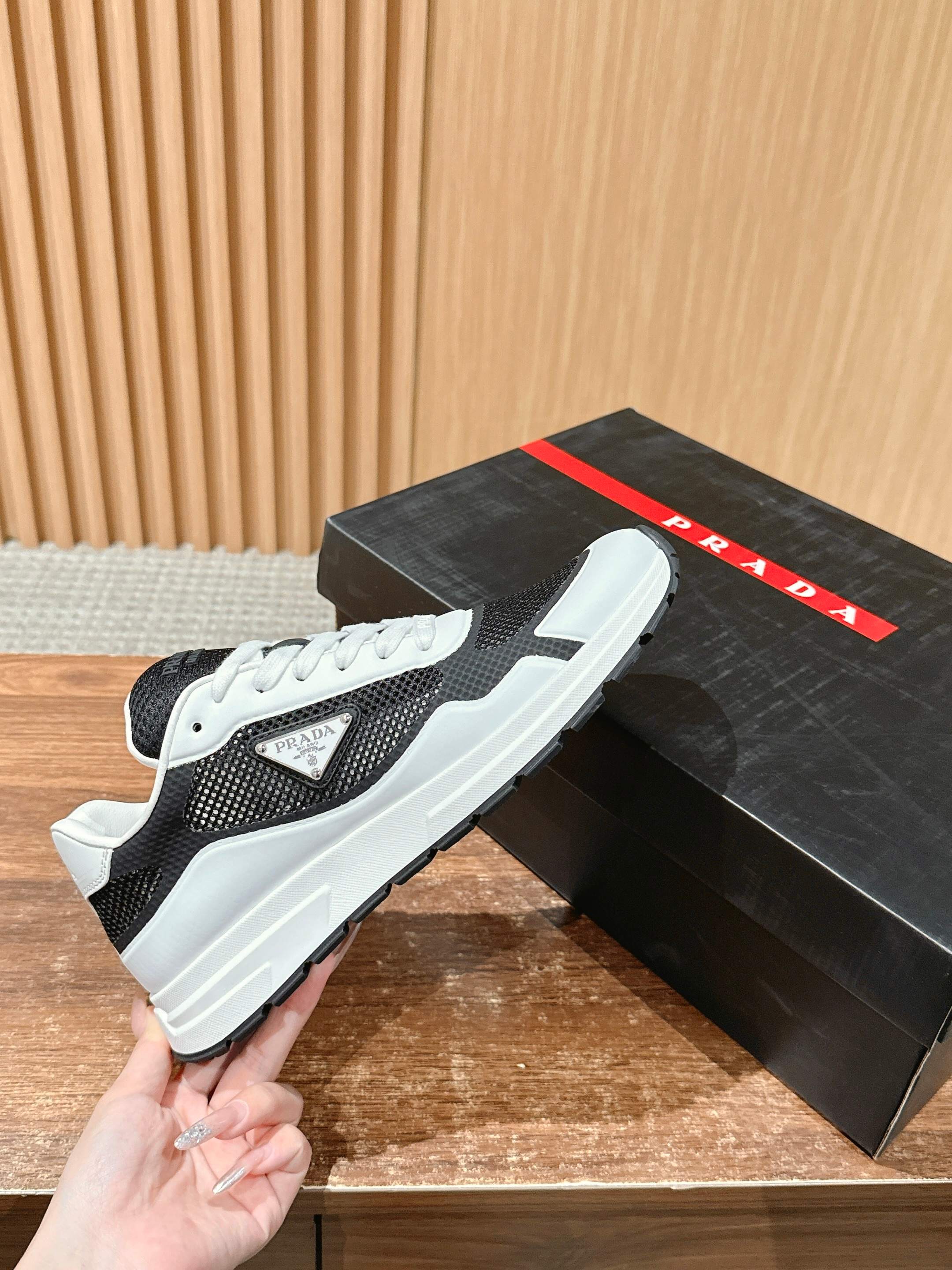 Black and white unisex sneakers with PRADA logo patch, held above display box
