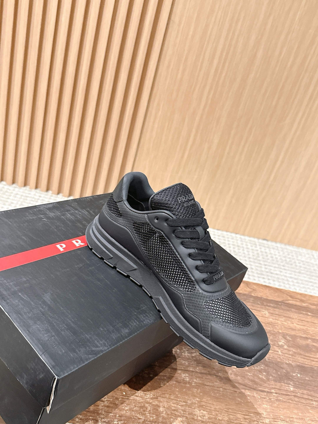 Black lace-up sneaker with textured upper and thick rubber sole on shoebox