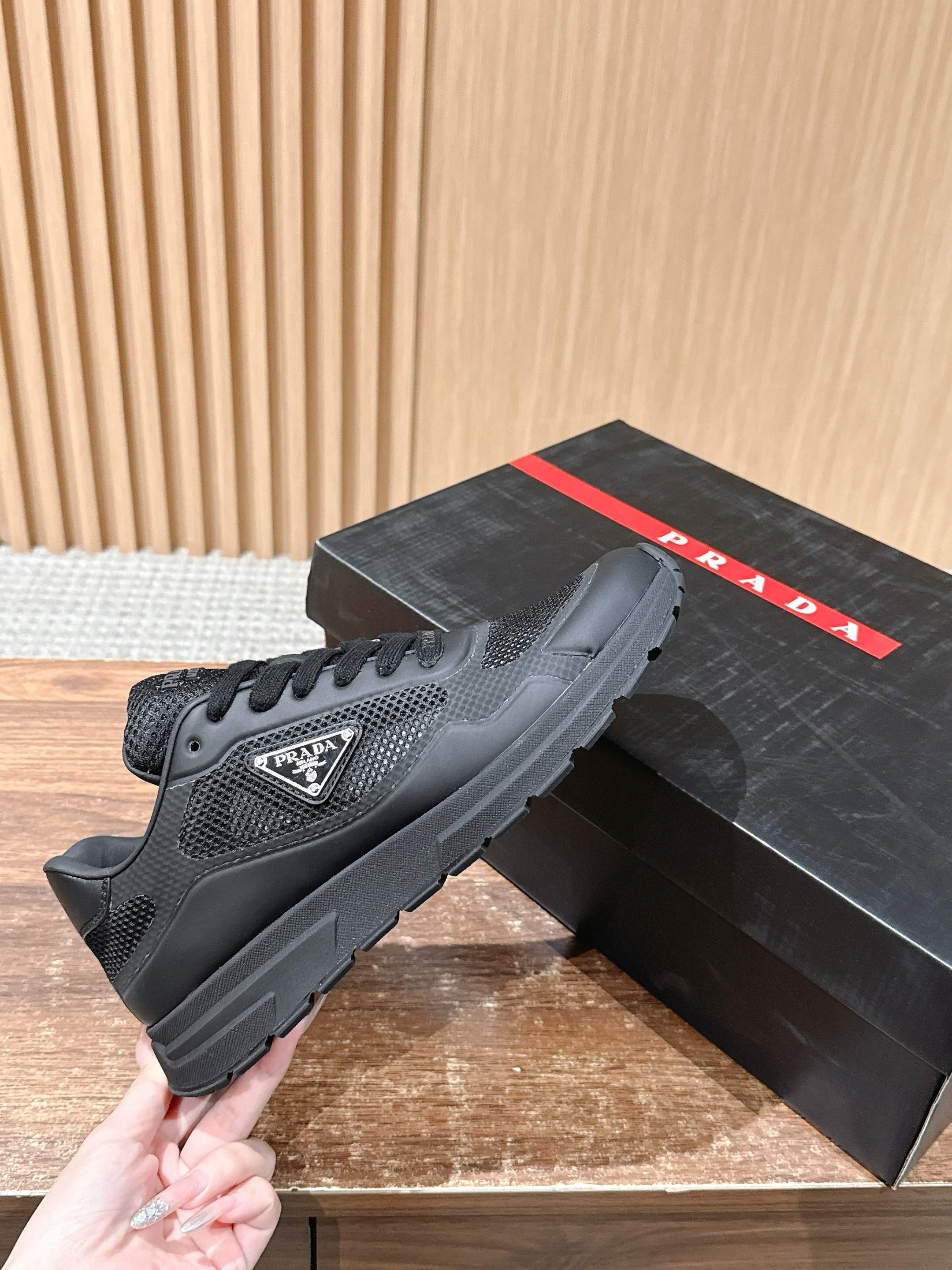 Black lace-up sneakers shown in hand, mesh upper and rubber tread sole