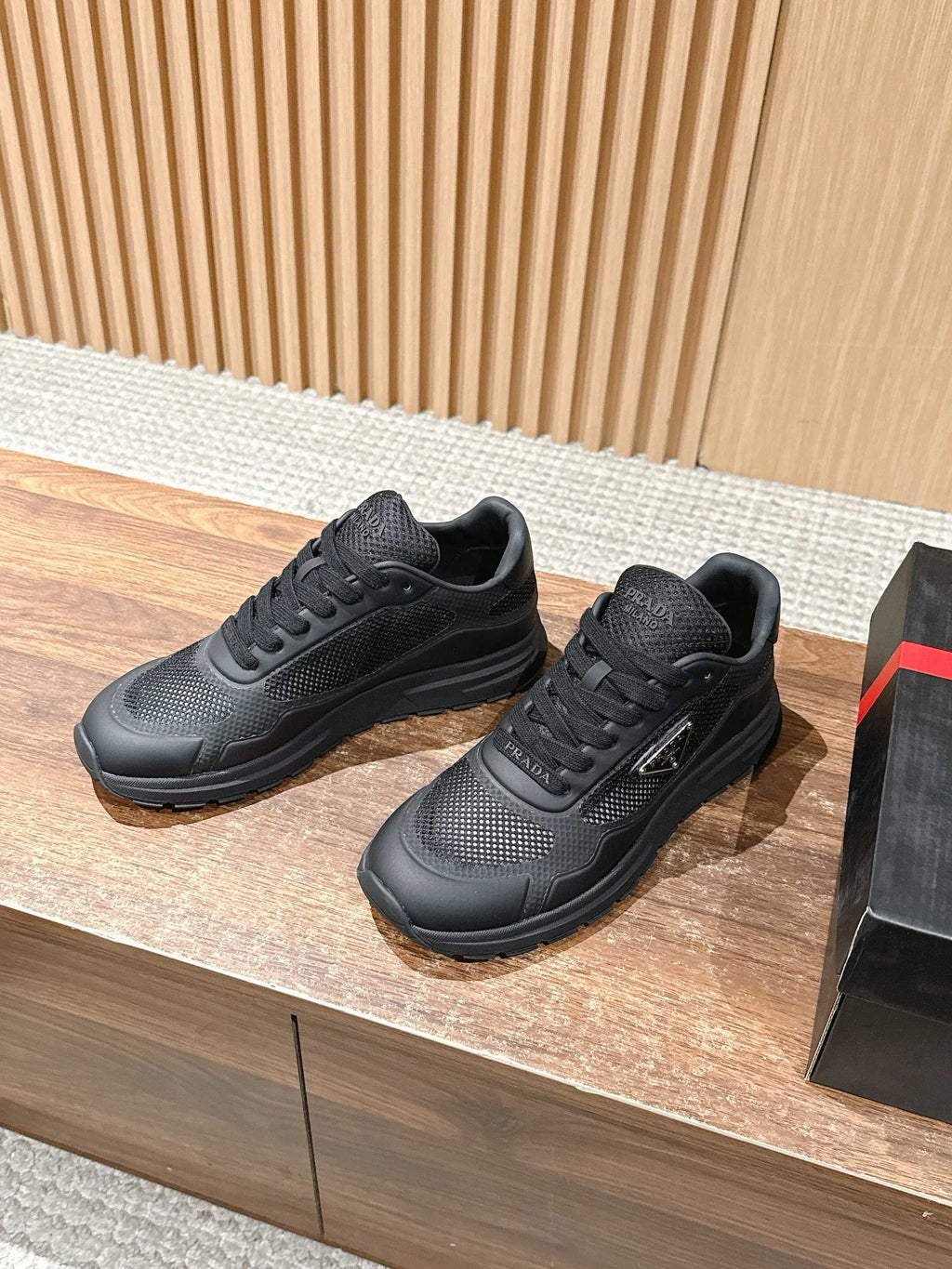 Black lace-up sneakers on box, mesh panels and chunky rubber sole visible