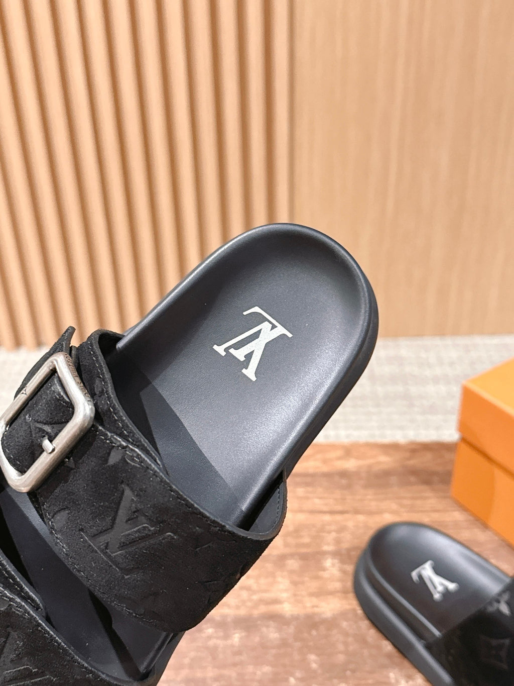Close-up of black monogram slide sandal with silver buckle strap and logo footbed