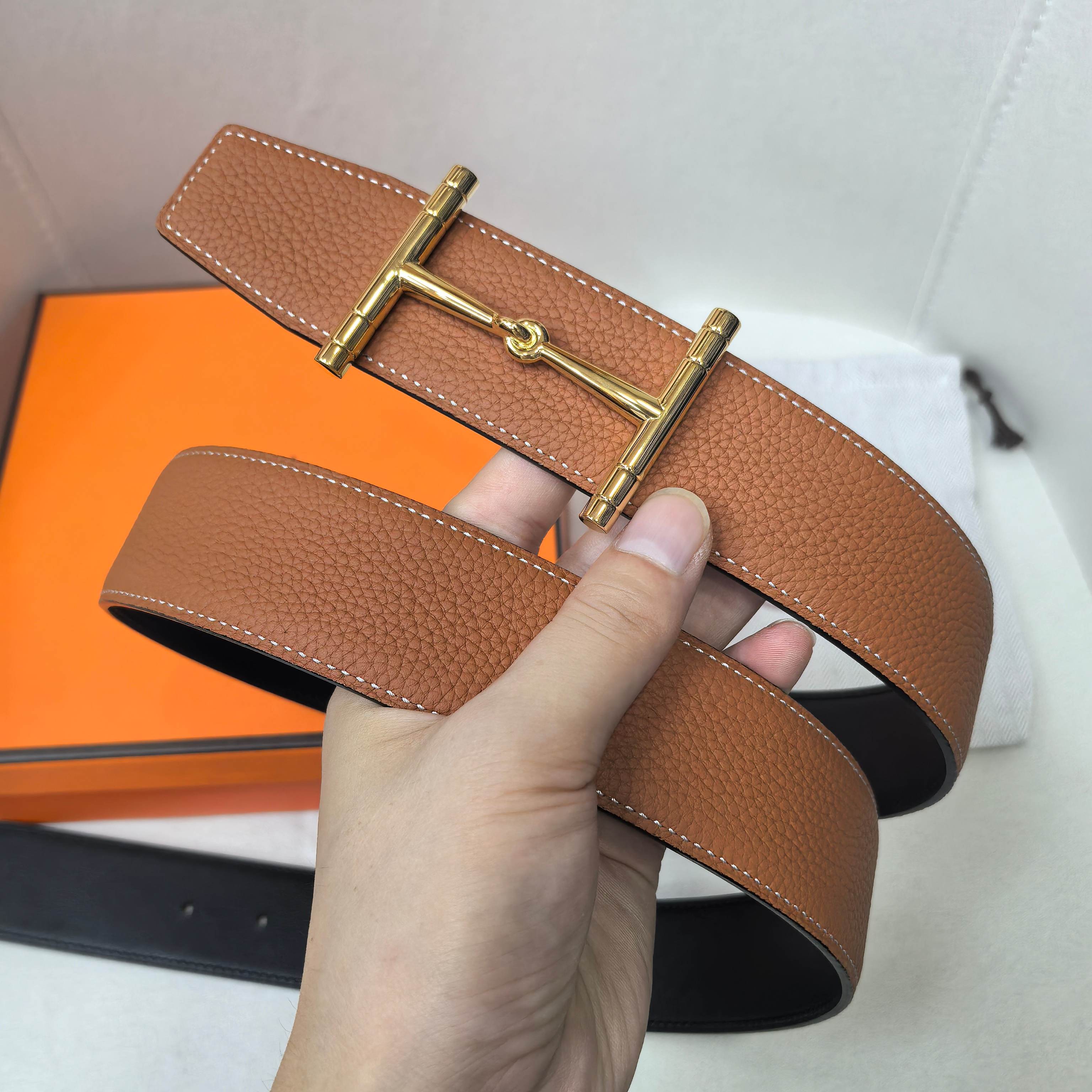 Brown leather belt with gold-tone buckle and keeper end, held in hand