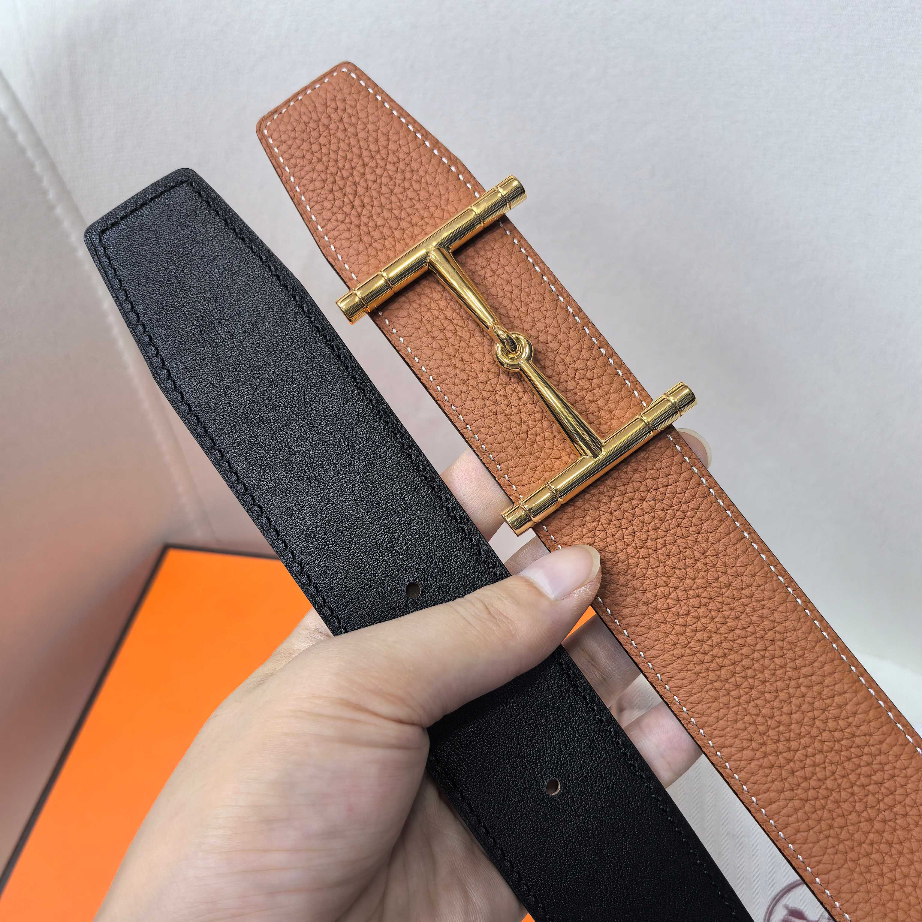 Brown and black leather belts with gold-tone buckle, shown side by side