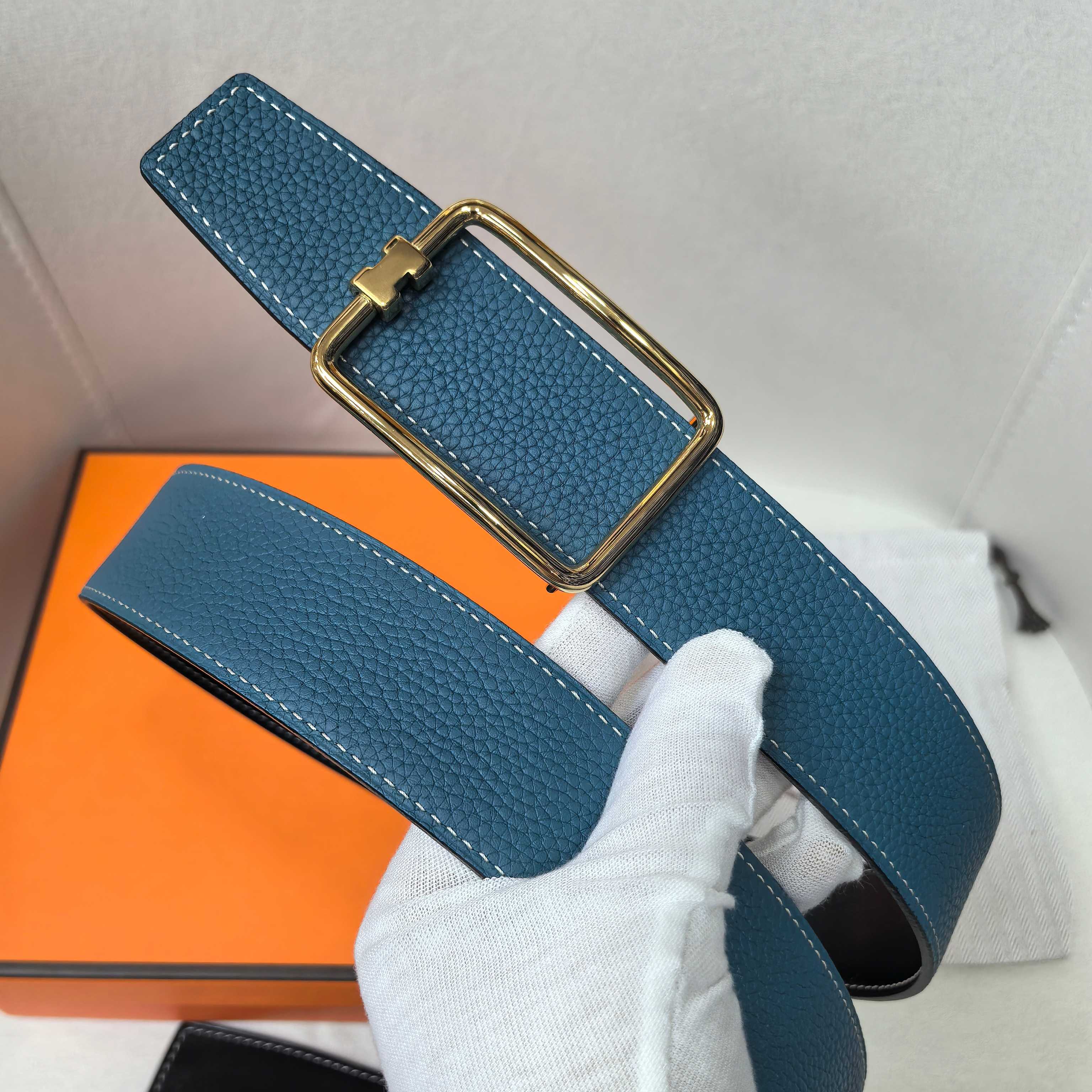 Leather belt, blue textured strap with gold rectangular buckle and stitching.