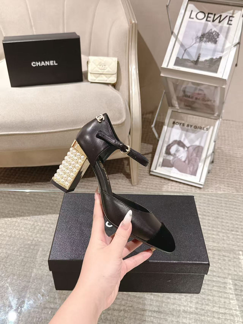 Women's black heeled sandal held up by hand, pearl block heel detail