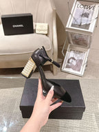 Women's black heeled sandal held up by hand, pearl block heel detail