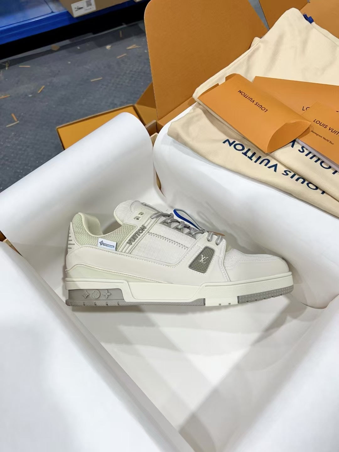 White Louis Vuitton trainer shoe, side view with LV logo and blue lace stripe.