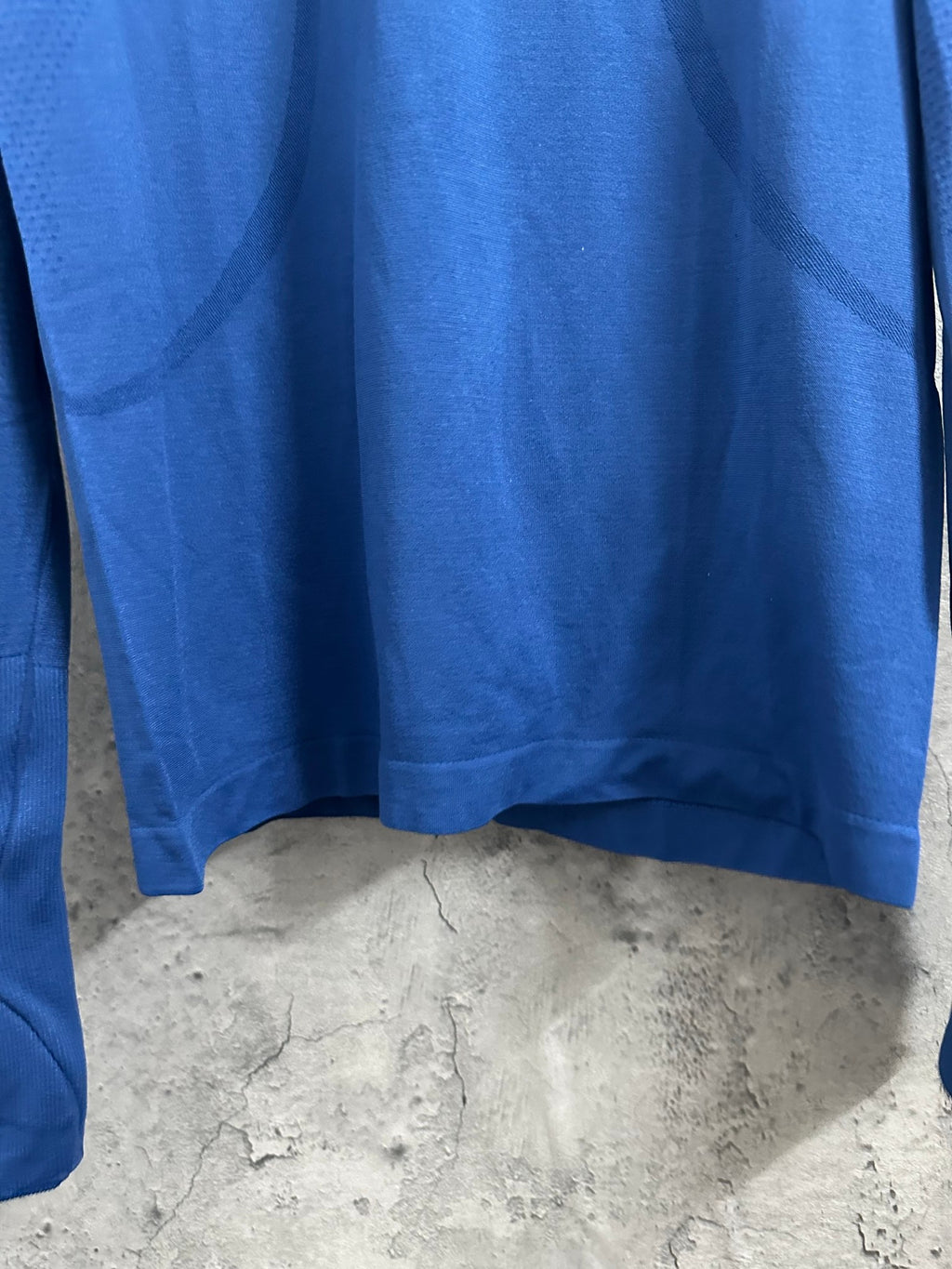 Blue long-sleeve T-shirt hem with curved bottom and underarm seam.