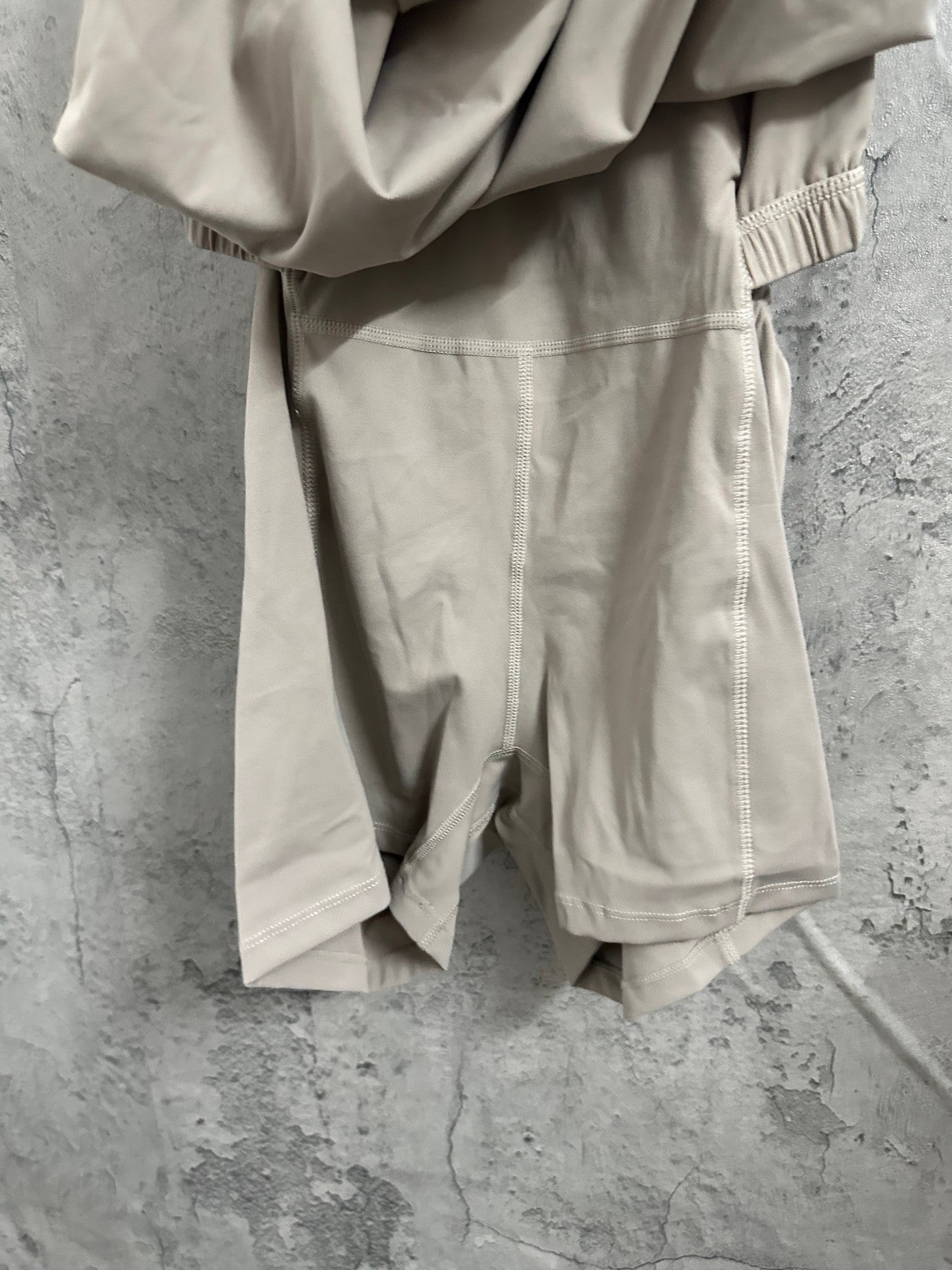 Light beige romper close-up of side seams, elastic leg cuffs, and gathered fabric