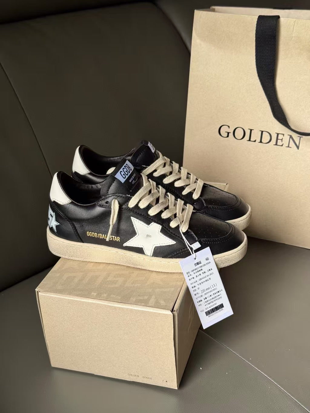 Black lace-up sneakers with white star accents and beige sole, shown on box