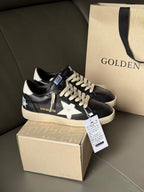 Black lace-up sneakers with white star accents and beige sole, shown on box