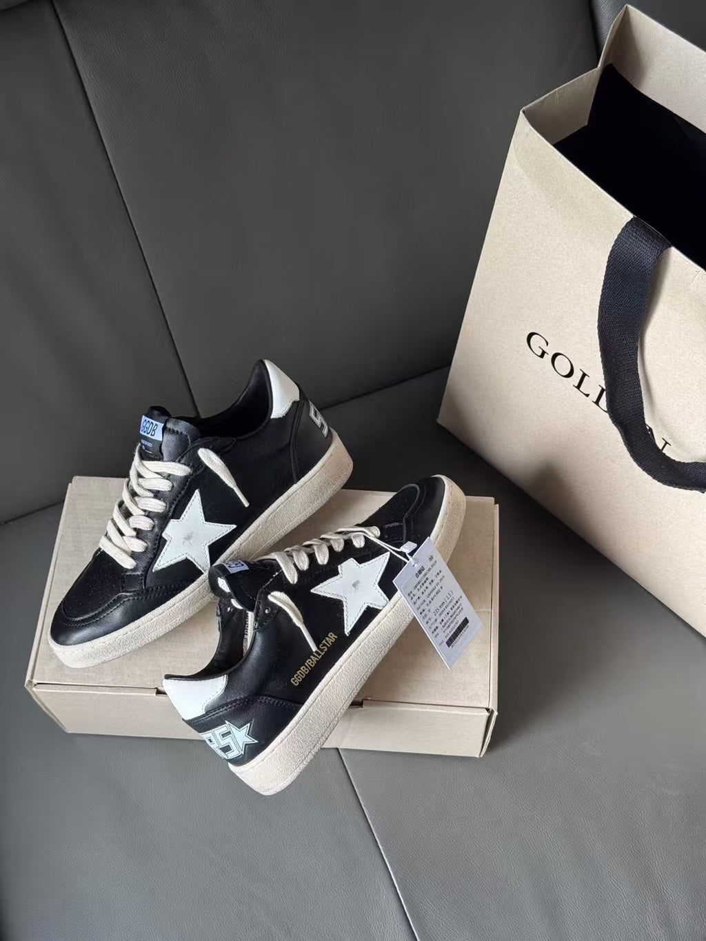 Black low-top sneakers with white star and patterned heel patch, on shoebox
