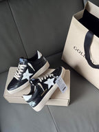 Black low-top sneakers with white star and patterned heel patch, on shoebox