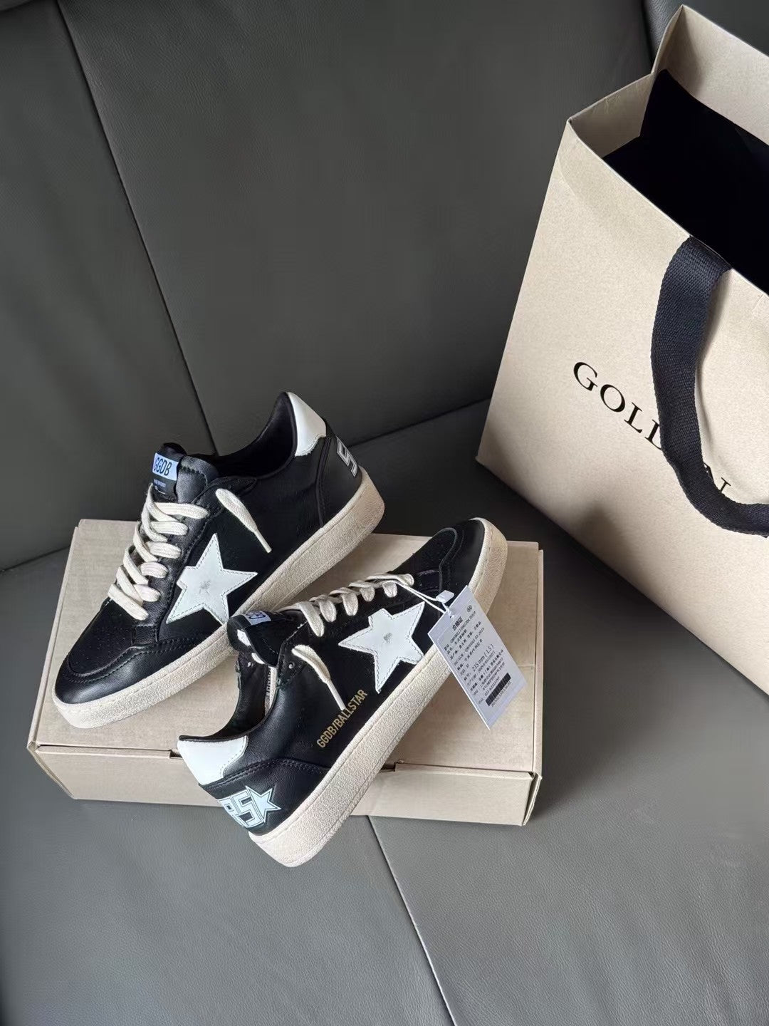 Black low-top sneakers with white star and patterned heel patch, on shoebox