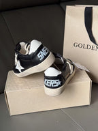 Black sneakers with white laces, heel tab showing star mark, beige sole