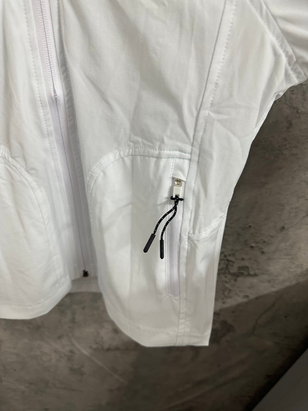 White jacket sleeve with pocket flap and metal zipper pull, drawstring cord