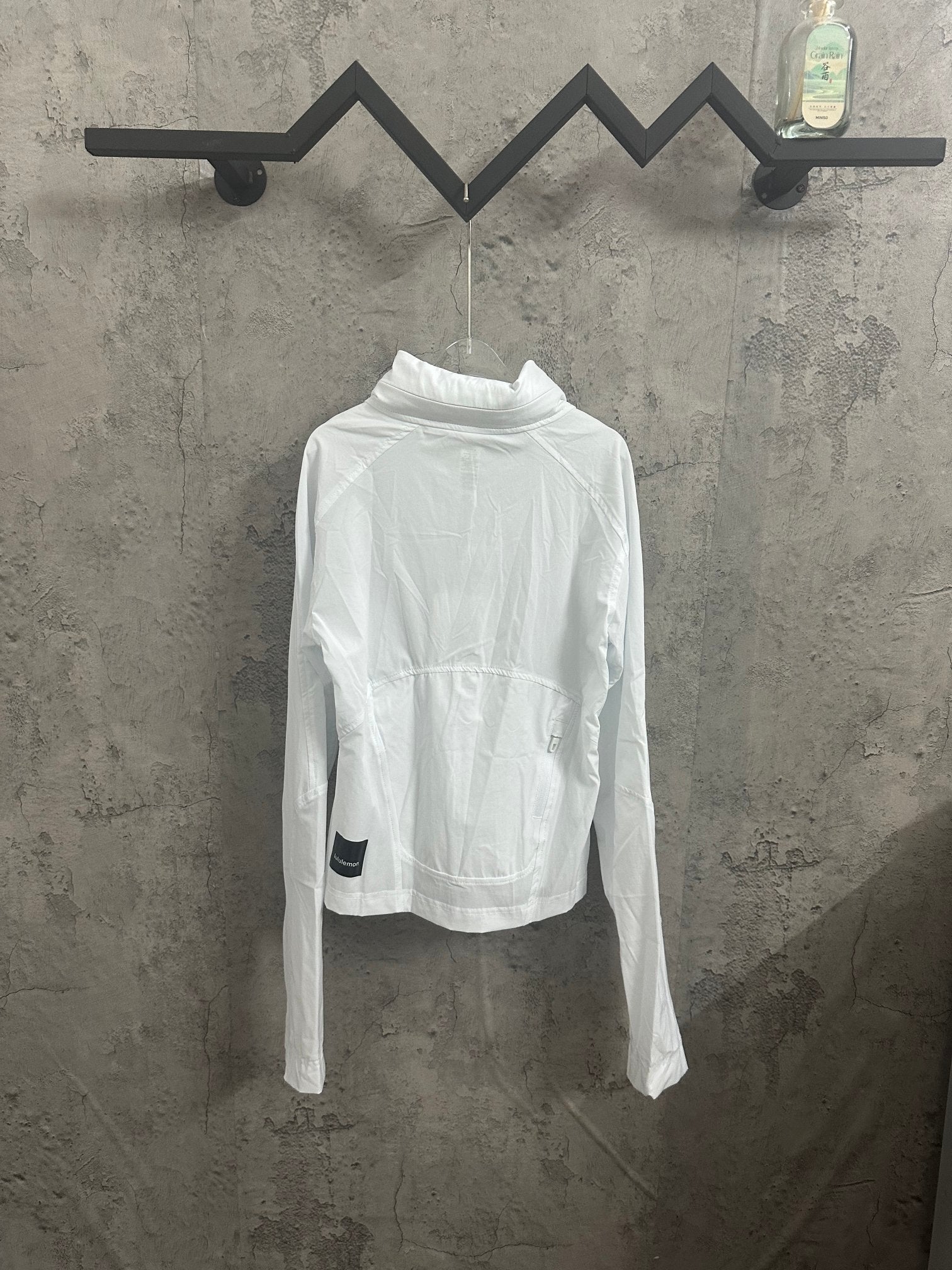 White mock-neck zip jacket with drawstring accents on the front, displayed on a hanger.