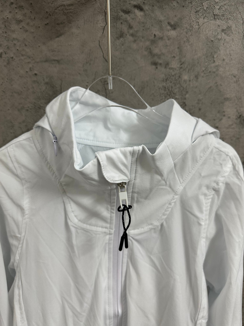 White jacket close-up at the stand collar with central zipper and black drawstring ties.