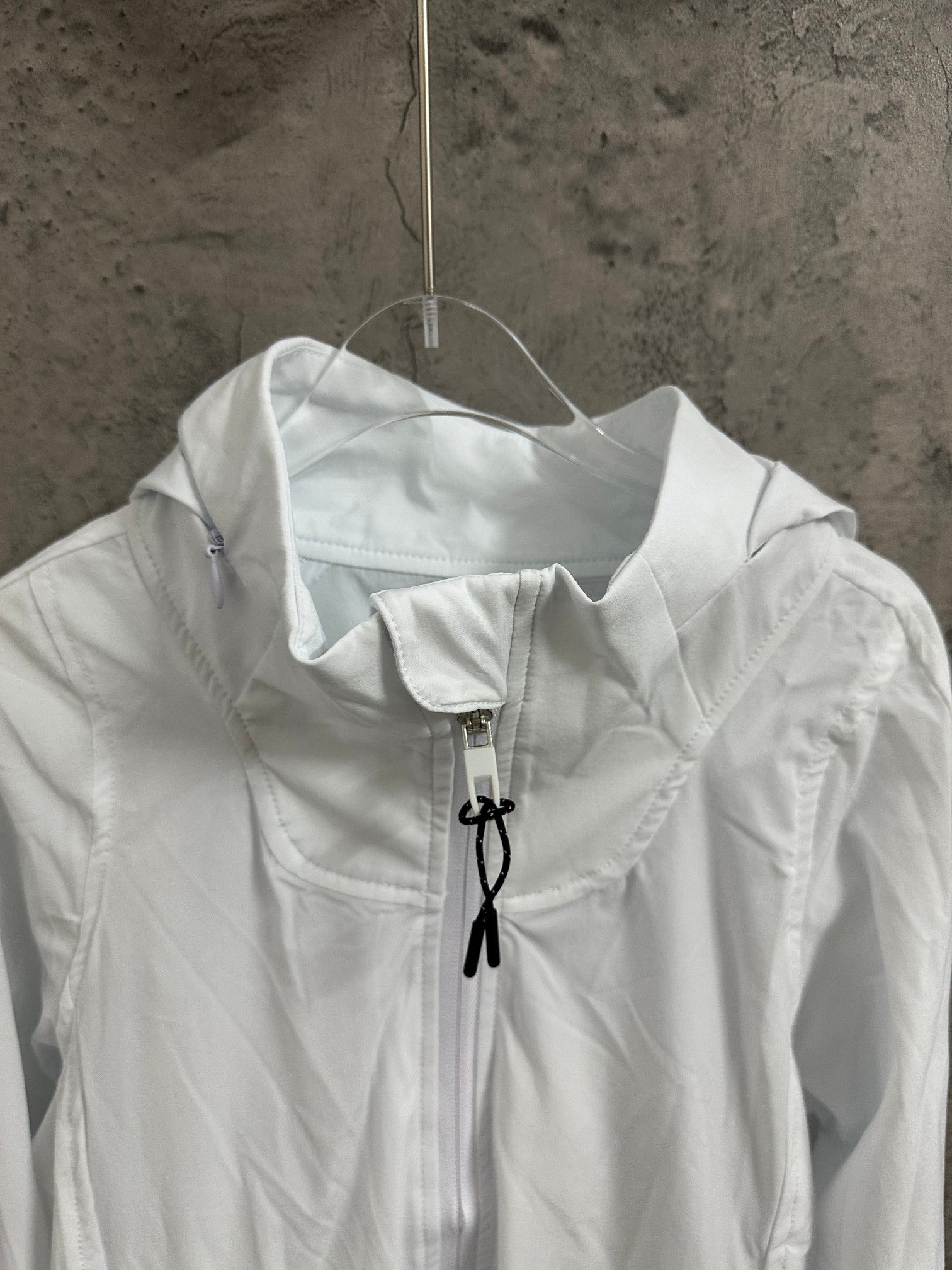 White jacket close-up at the stand collar with central zipper and black drawstring ties.