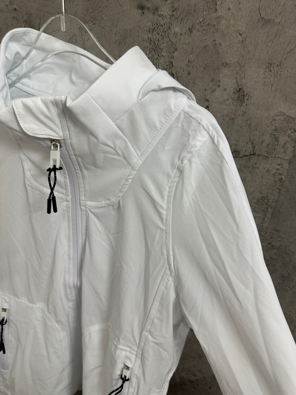 White zip jacket with stand collar and long sleeves, shown from the side on a hanger.