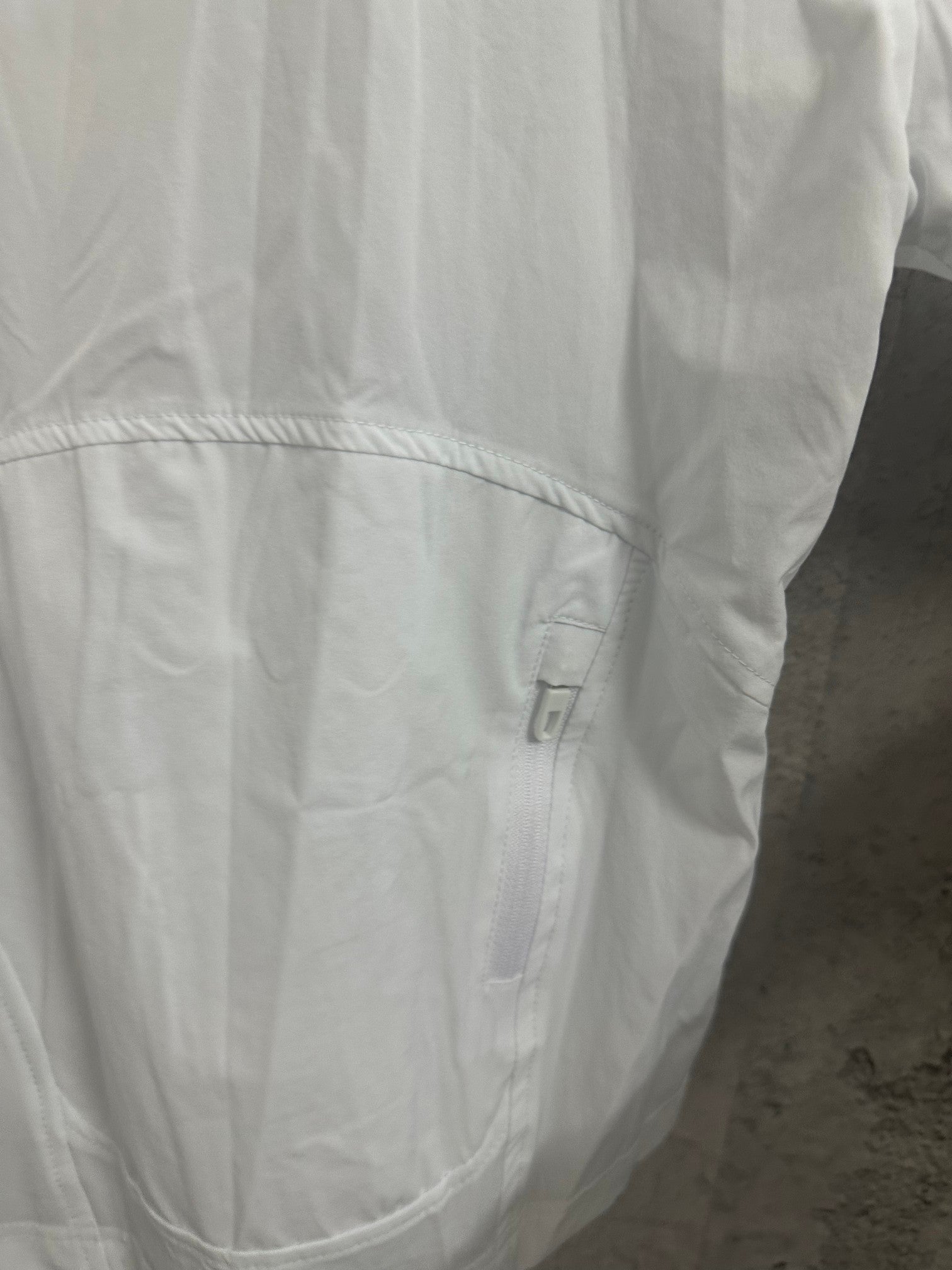 White jacket close-up of back yoke seam with small pocket area and zipper pull.
