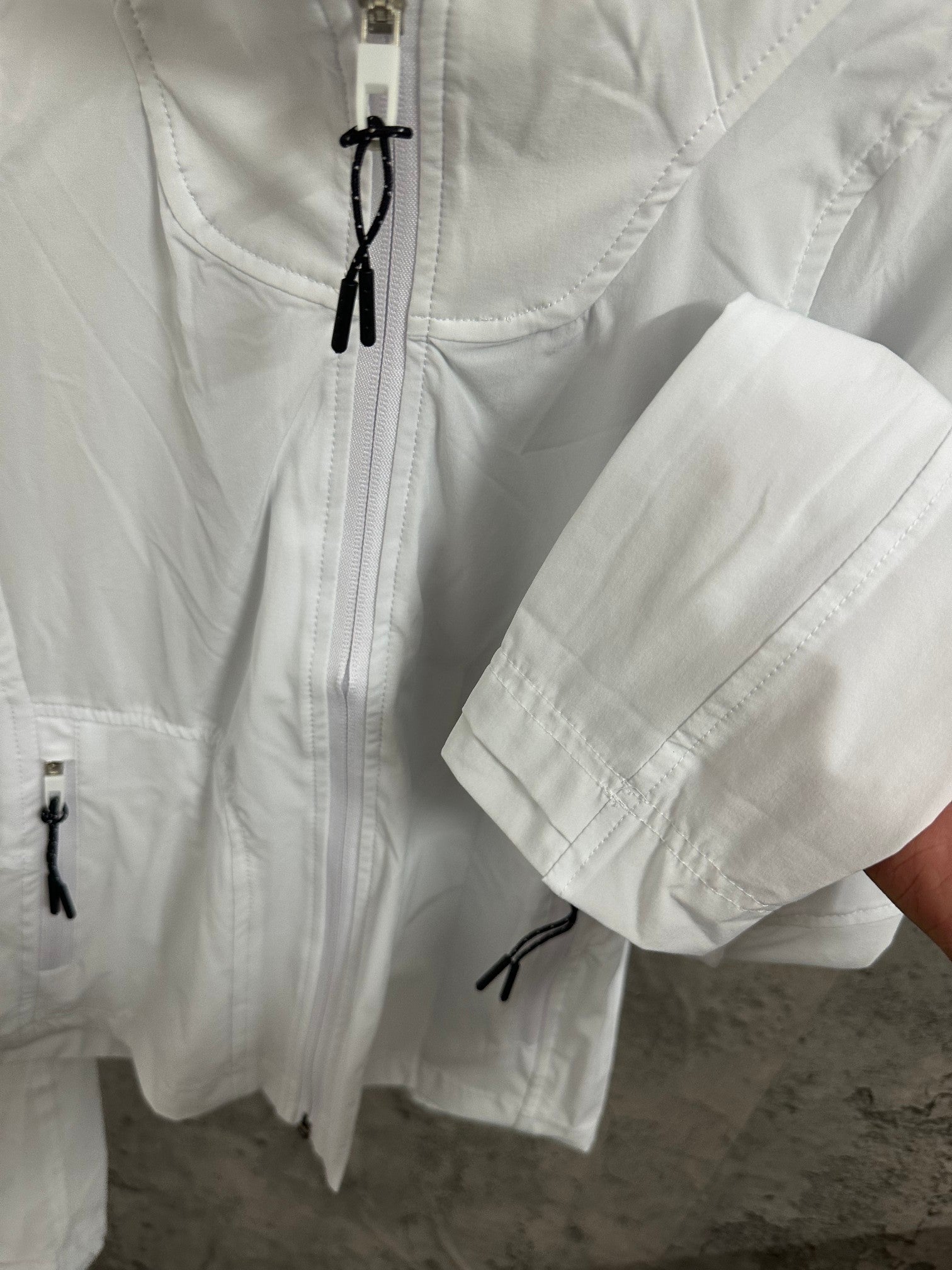 White jacket with front drawstring pulls, side pockets, and long sleeves