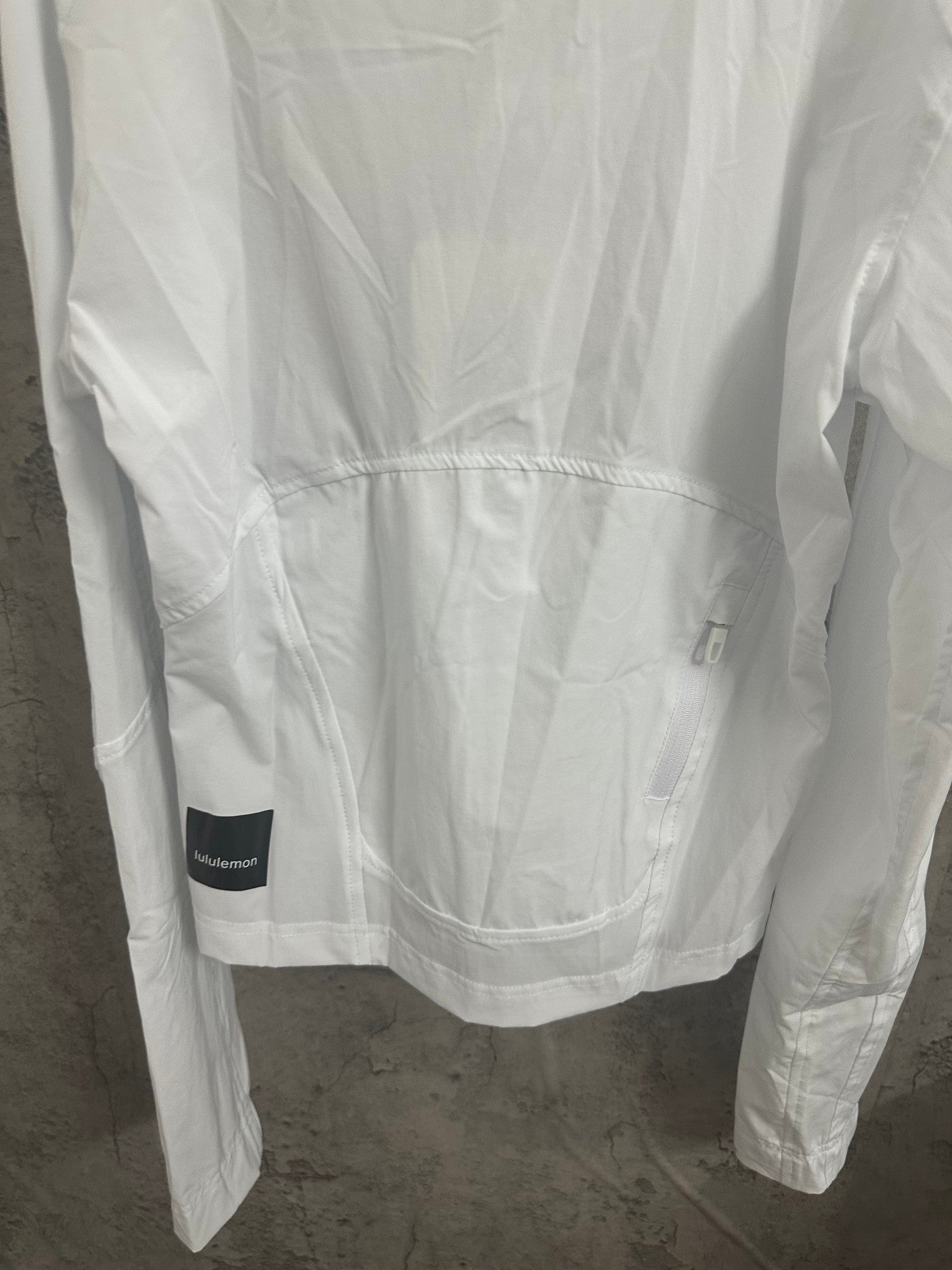White jacket back view with curved hem and logo patch on lower back