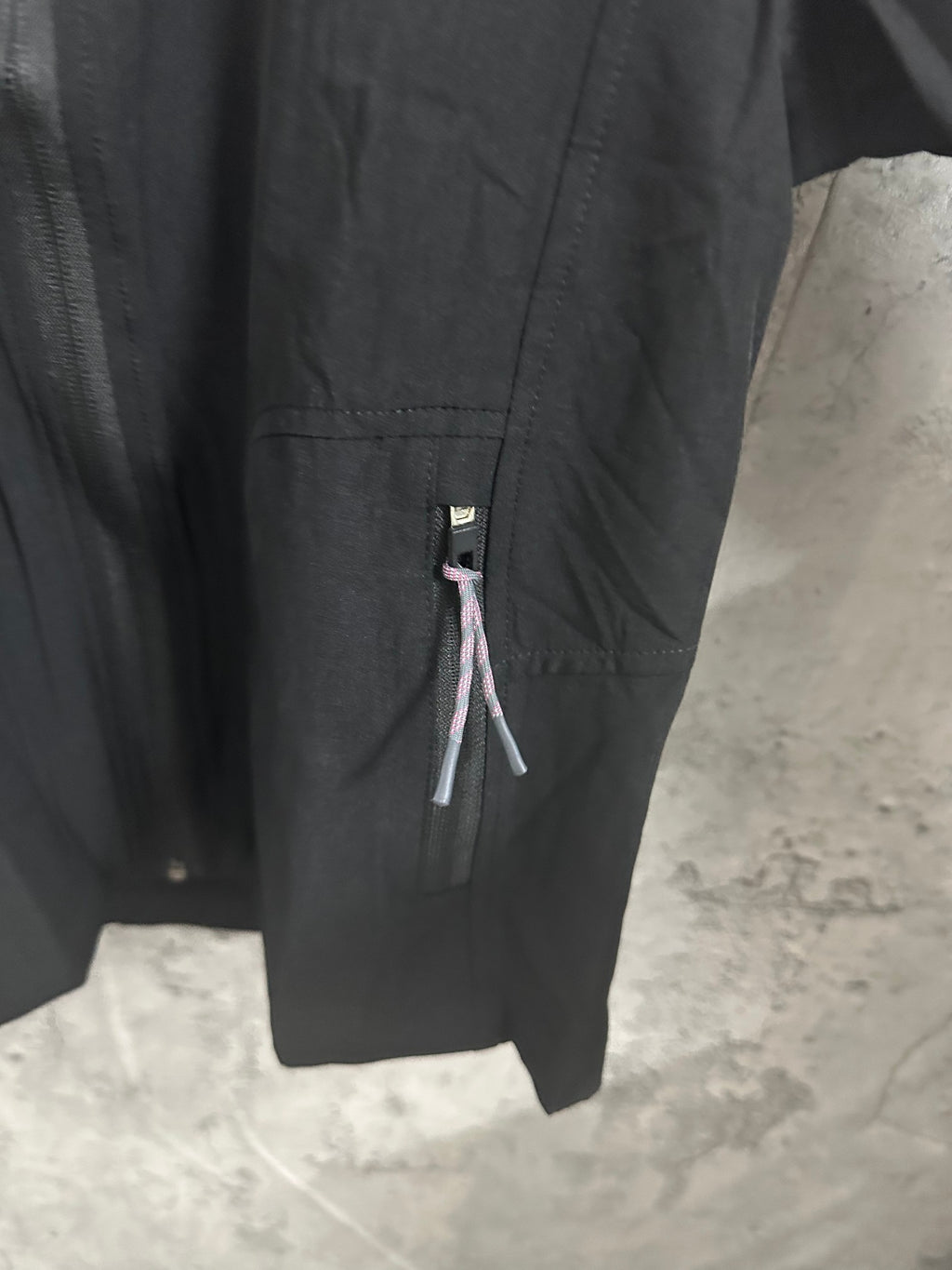 Black hooded jacket sleeve and side zipper pocket detail with logo tab
