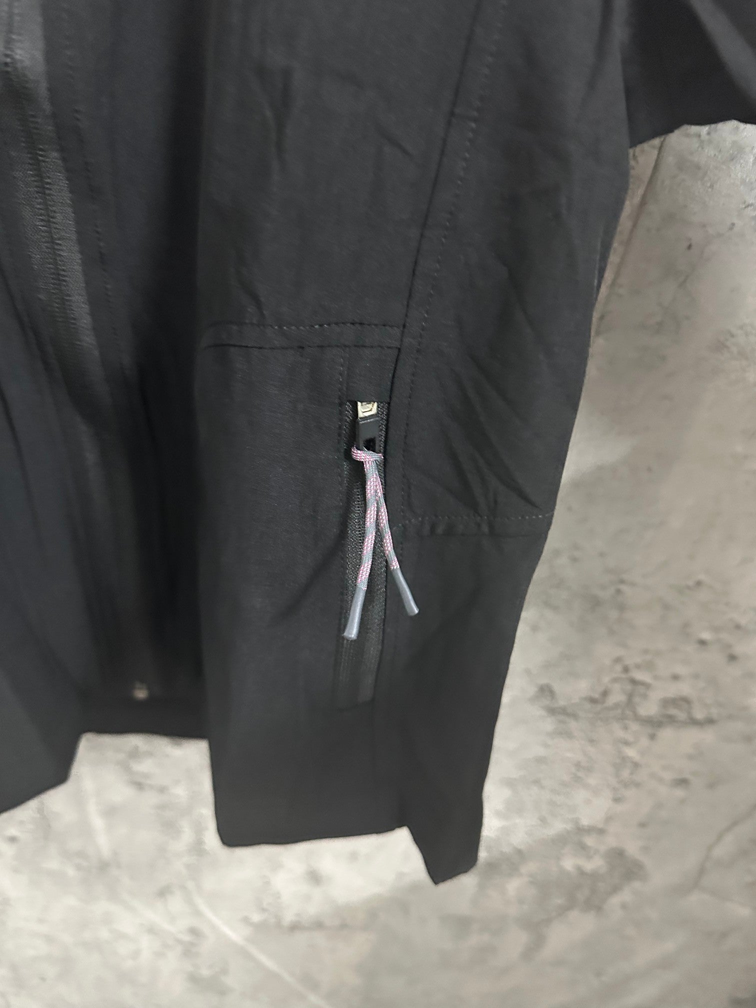 Black hooded jacket sleeve and side zipper pocket detail with logo tab