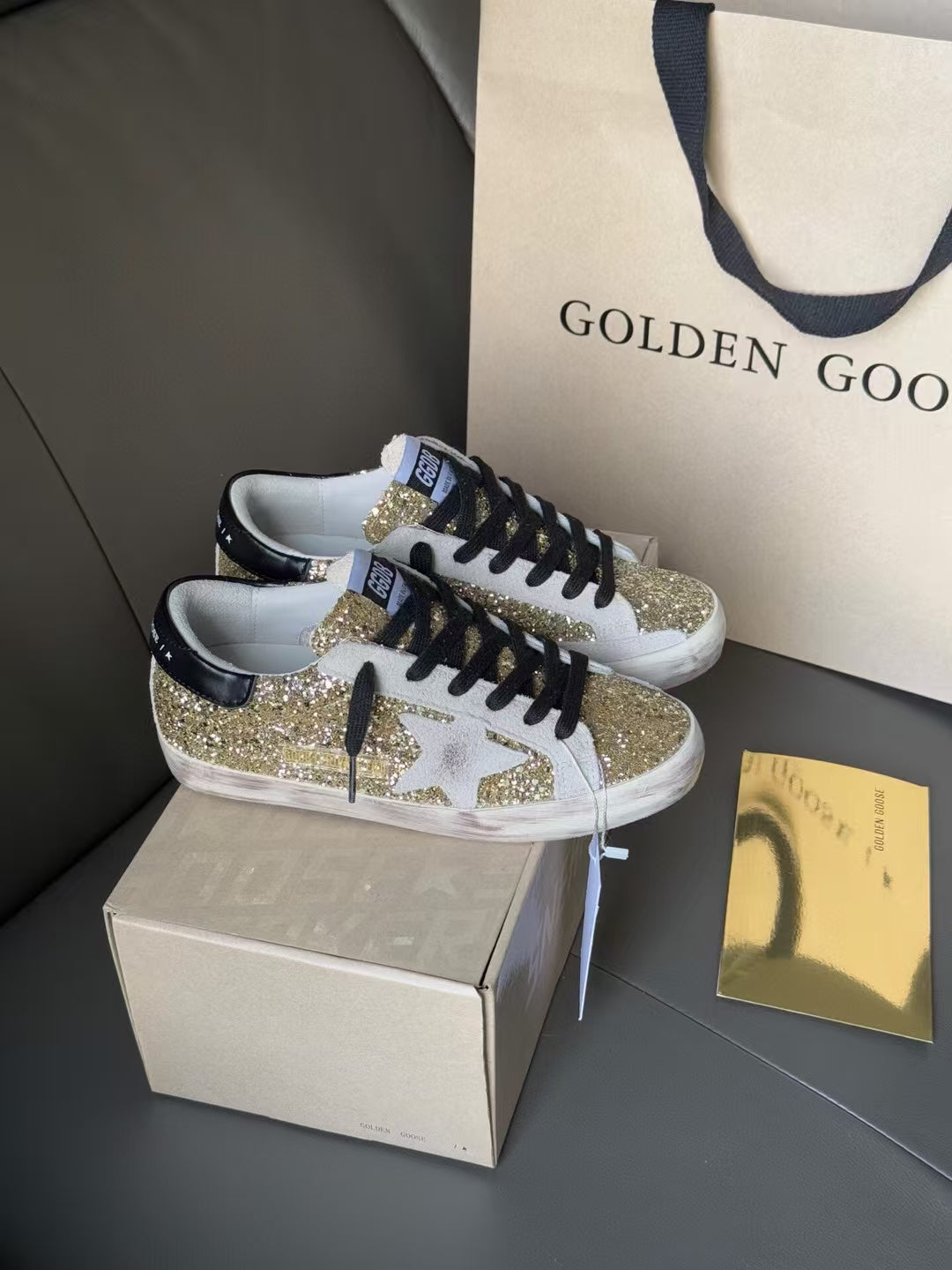 Golden Goose sneakers on a box, gold glitter uppers with black laces and white sole