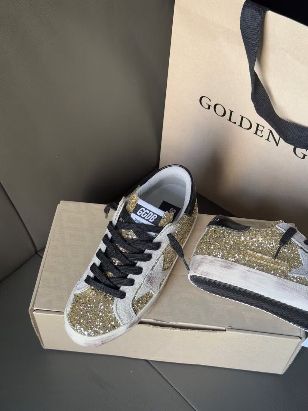 Golden Goose sneakers side view on box: gold glitter uppers, black laces, white sole