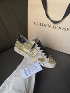 Golden Goose sneakers with gold glitter panels, black laces, and white sole