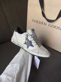 White low-top sneakers with blue star detail, lace-up front, on display box