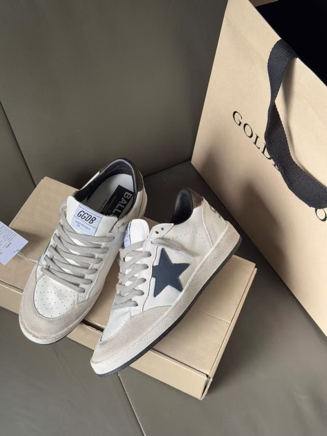 White leather sneakers with blue star and gray trim, lace-up, shown on shoeboxes
