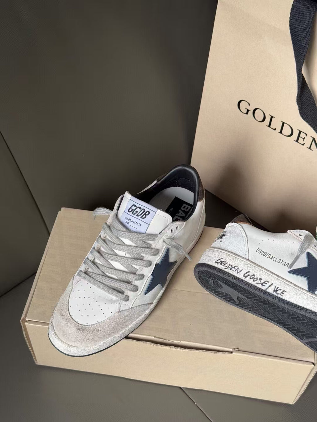 White low-top sneakers with blue star detail and gray sole, lace-up, on shoebox