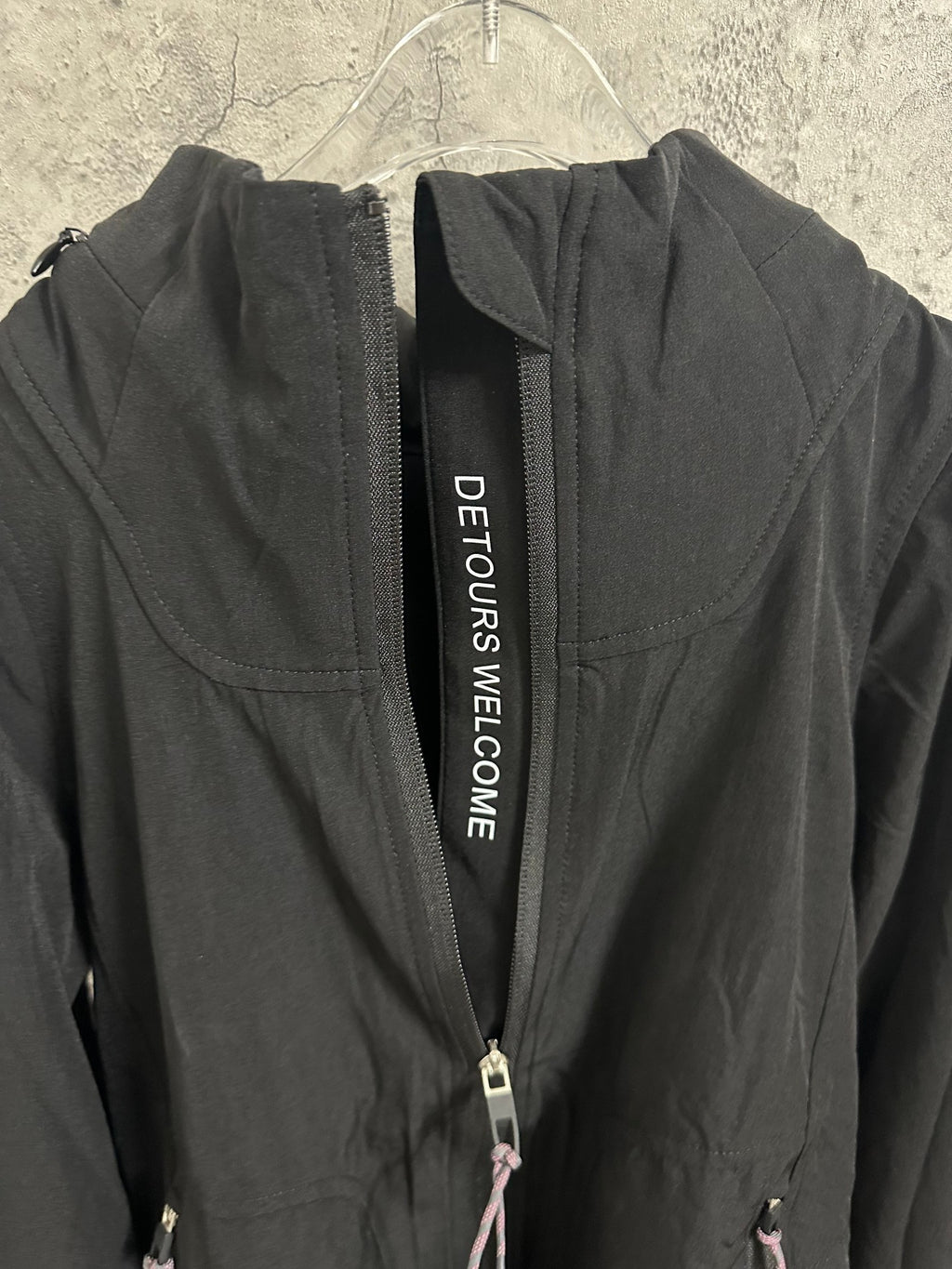 Black hooded jacket with DETOURS WELCOME text tape on zip placket
