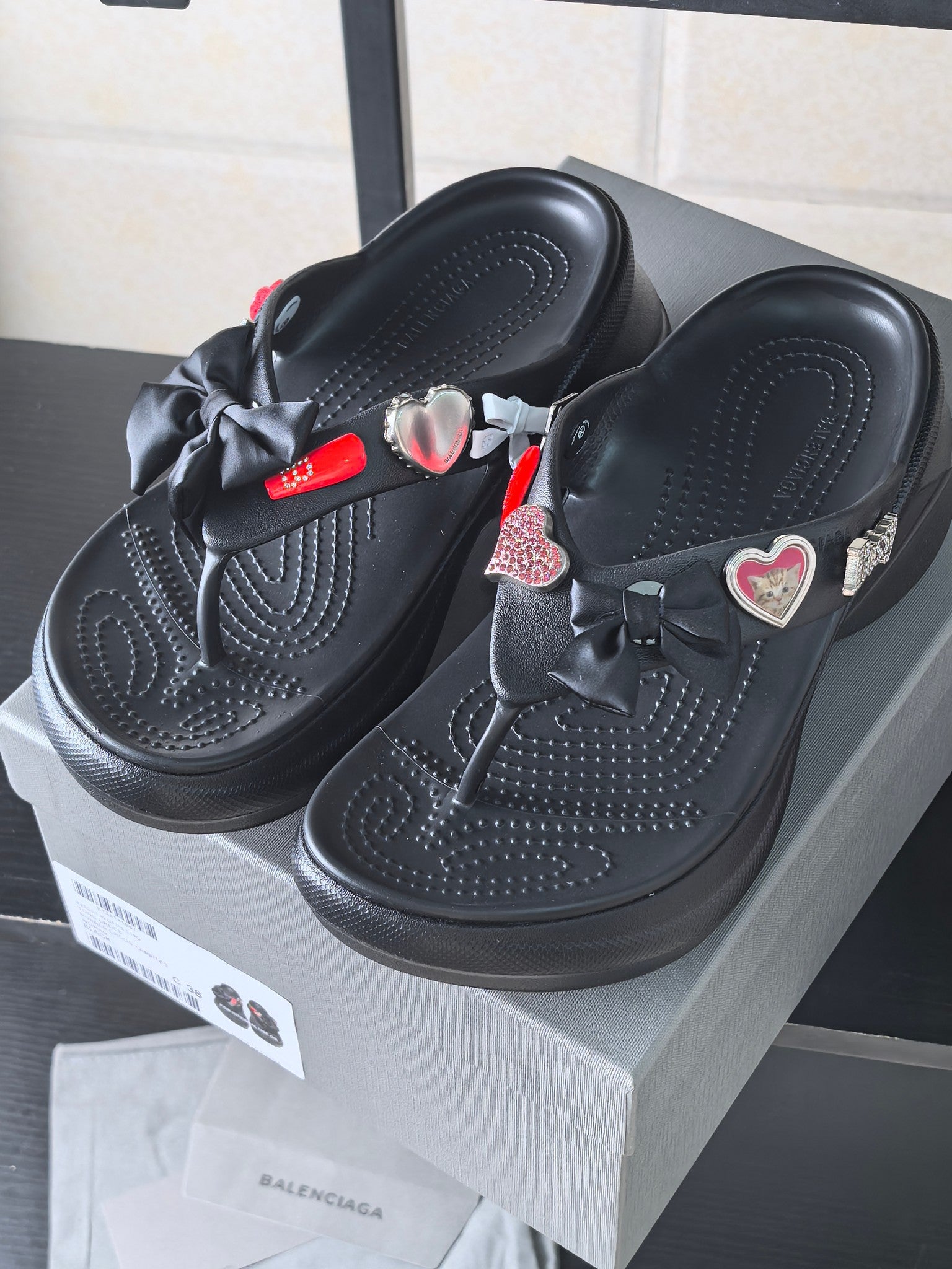 Black platform sandals with large bow at the toe and heart and logo charms