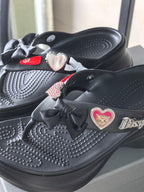 Black platform sandals with heart pins, bow ties, and textured perforated upper