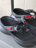 Black platform sandals showing bow ties and heart patch on the front strap
