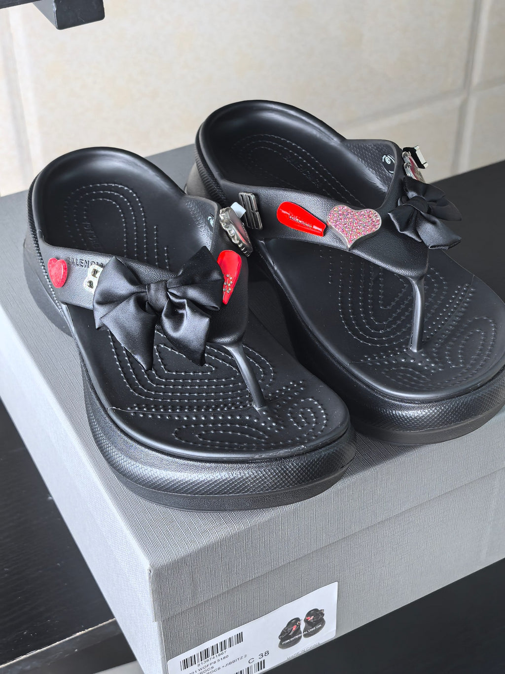 Pair of black platform sandals with perforated detailing, bows, and heart accents