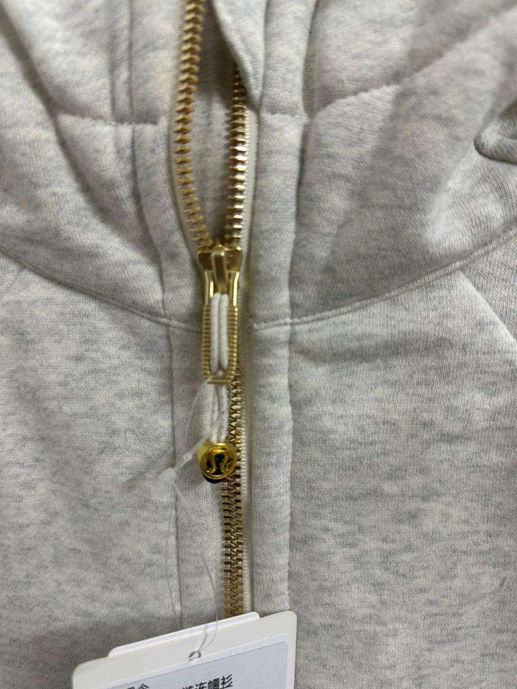 Close-up of gold zipper and metal pull on heather gray zip-up hoodie
