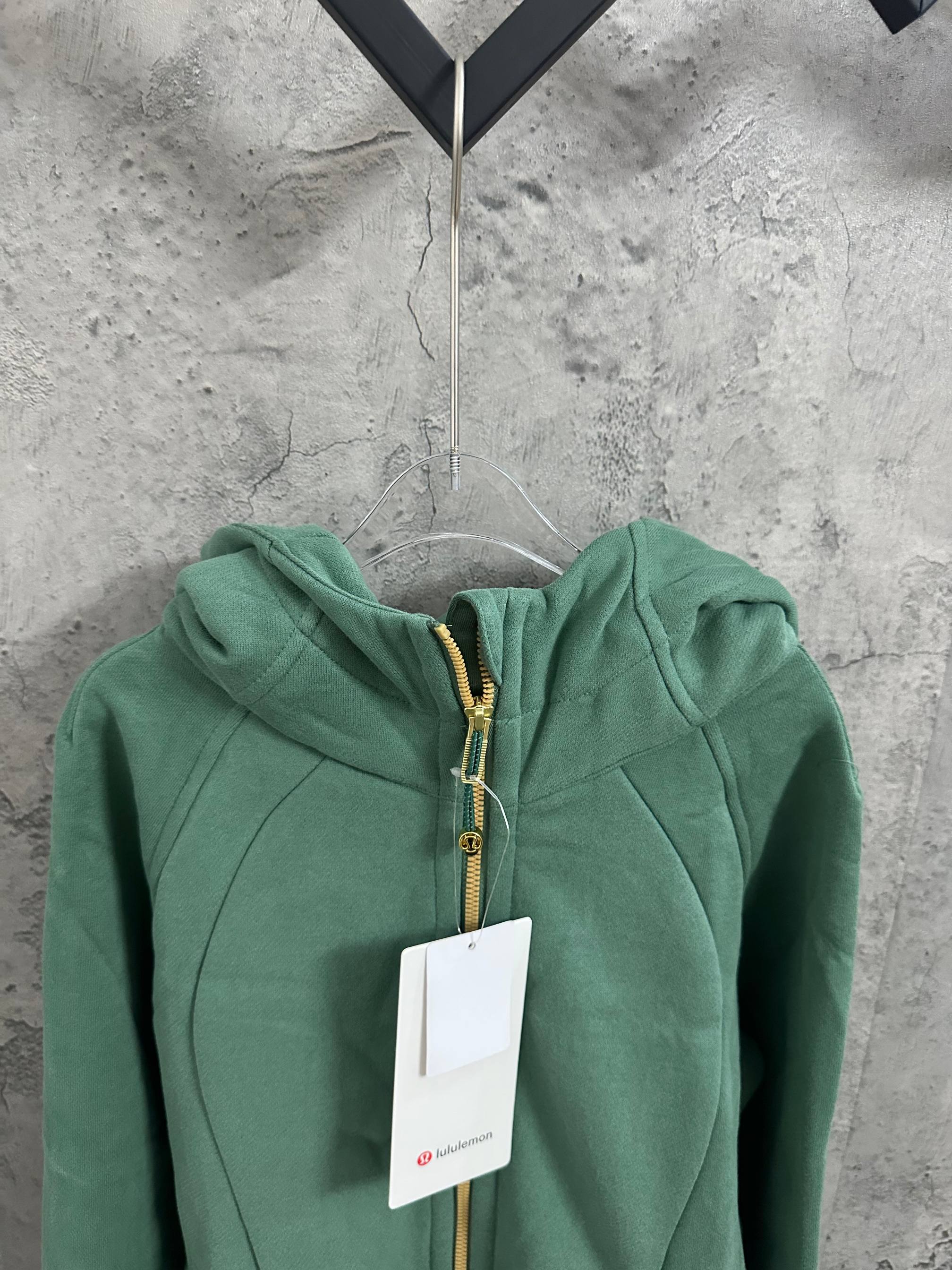 Green hooded zip jacket with front gold zipper and small logo tag