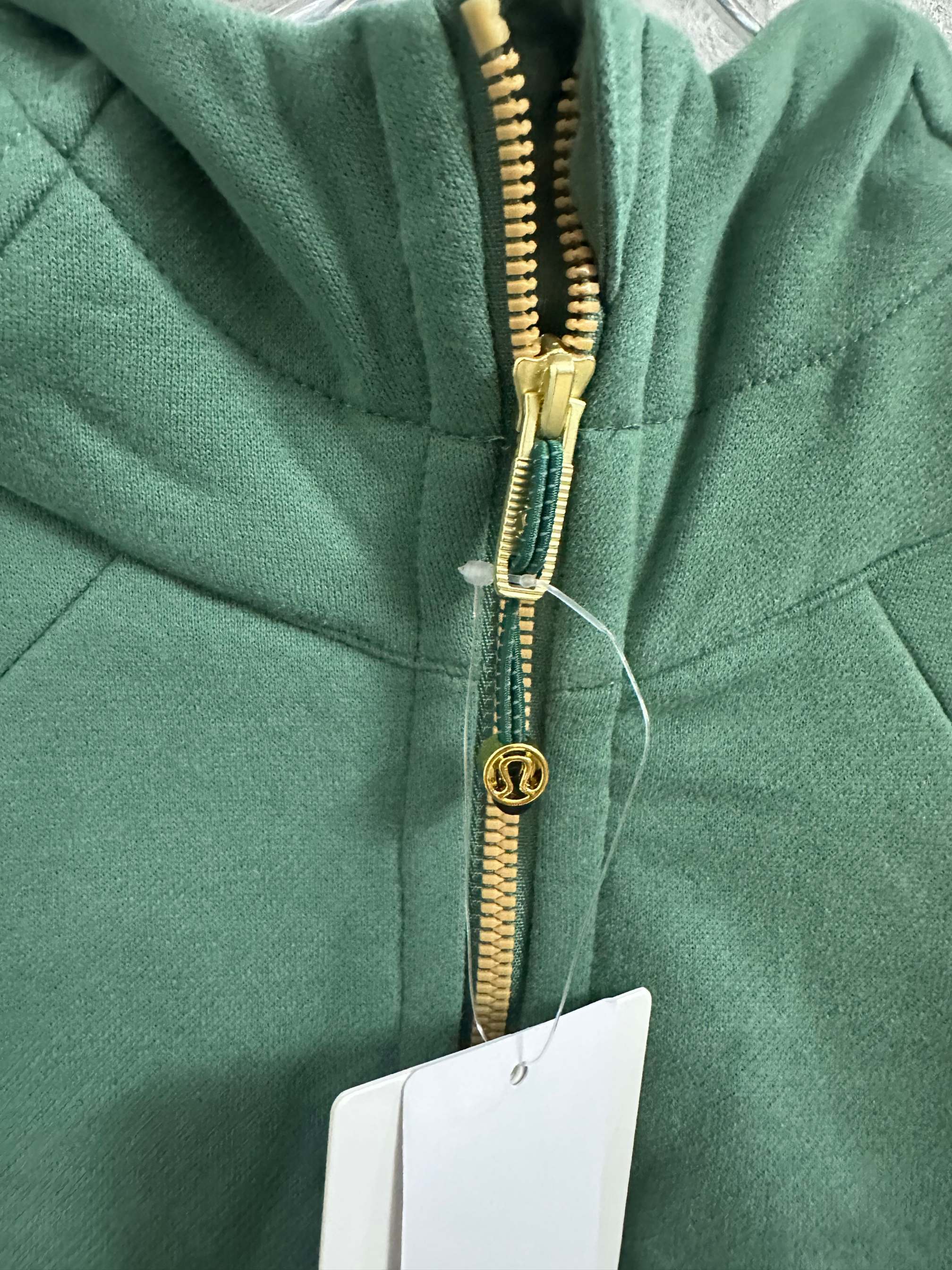 Green hooded zip jacket close-up of gold zipper with logo charm