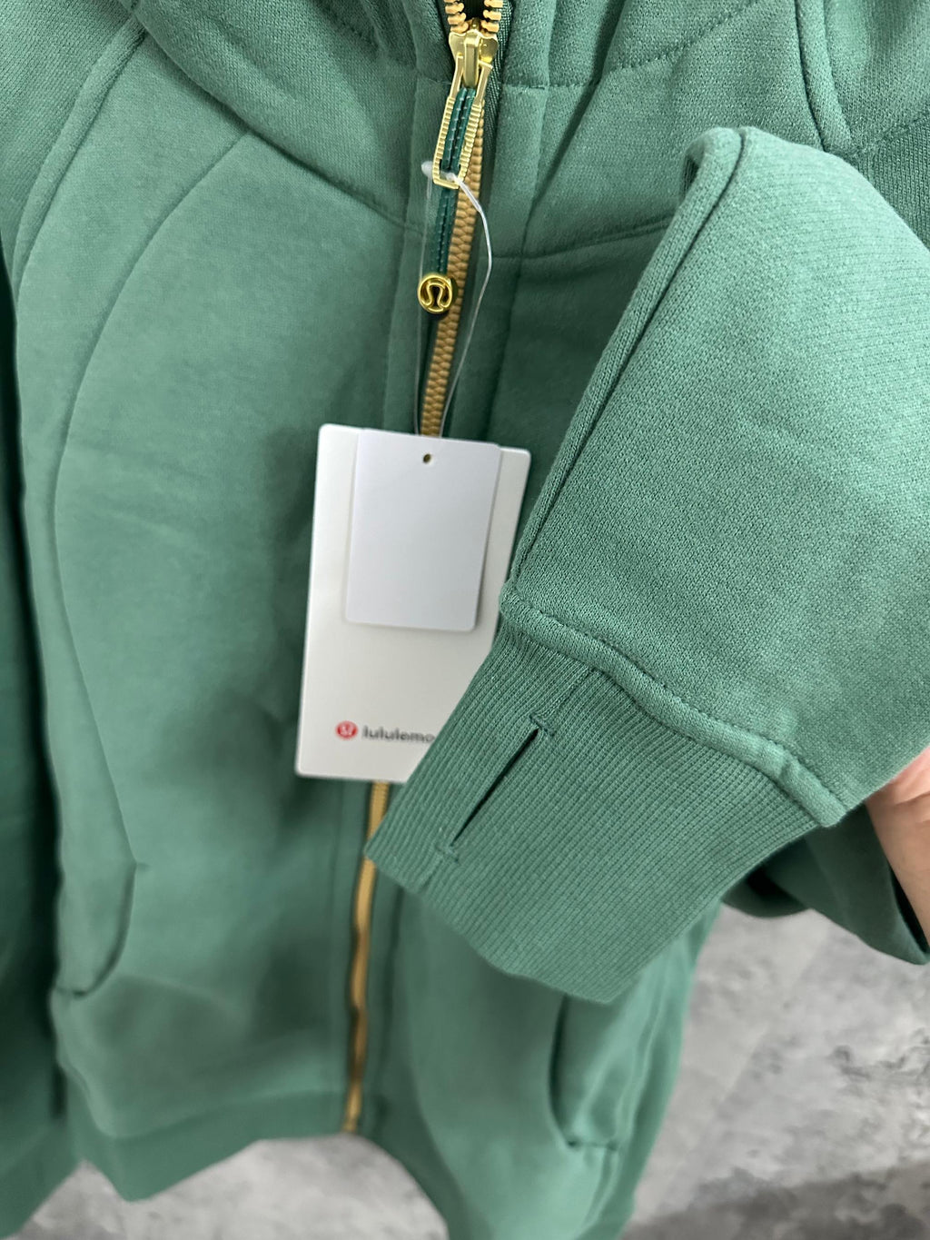 Green hooded zip jacket sleeve cuff with gold zipper edge and hanging tags