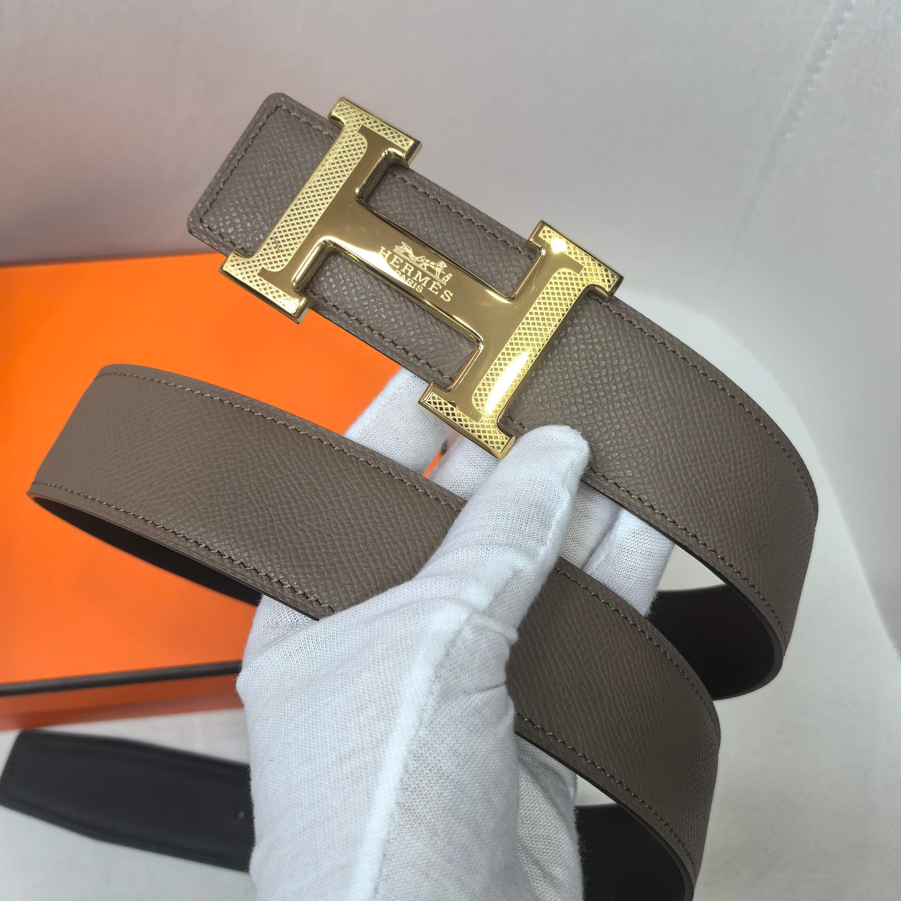 Taupe leather belt with gold H buckle and textured strap, wide keeper visible